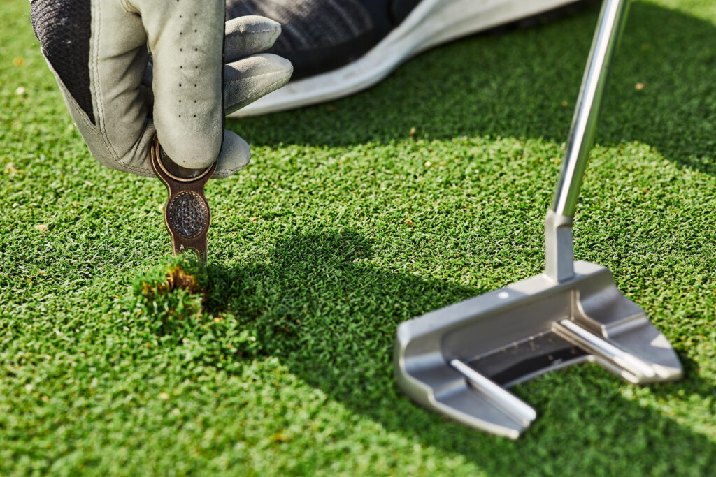 Golfer properly repair a divot mark on putting green using divot tool. Ball mark repair tool or divot tool on golf turf, close-up